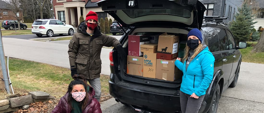 Three people standing in front of the back of the car filled with boxes