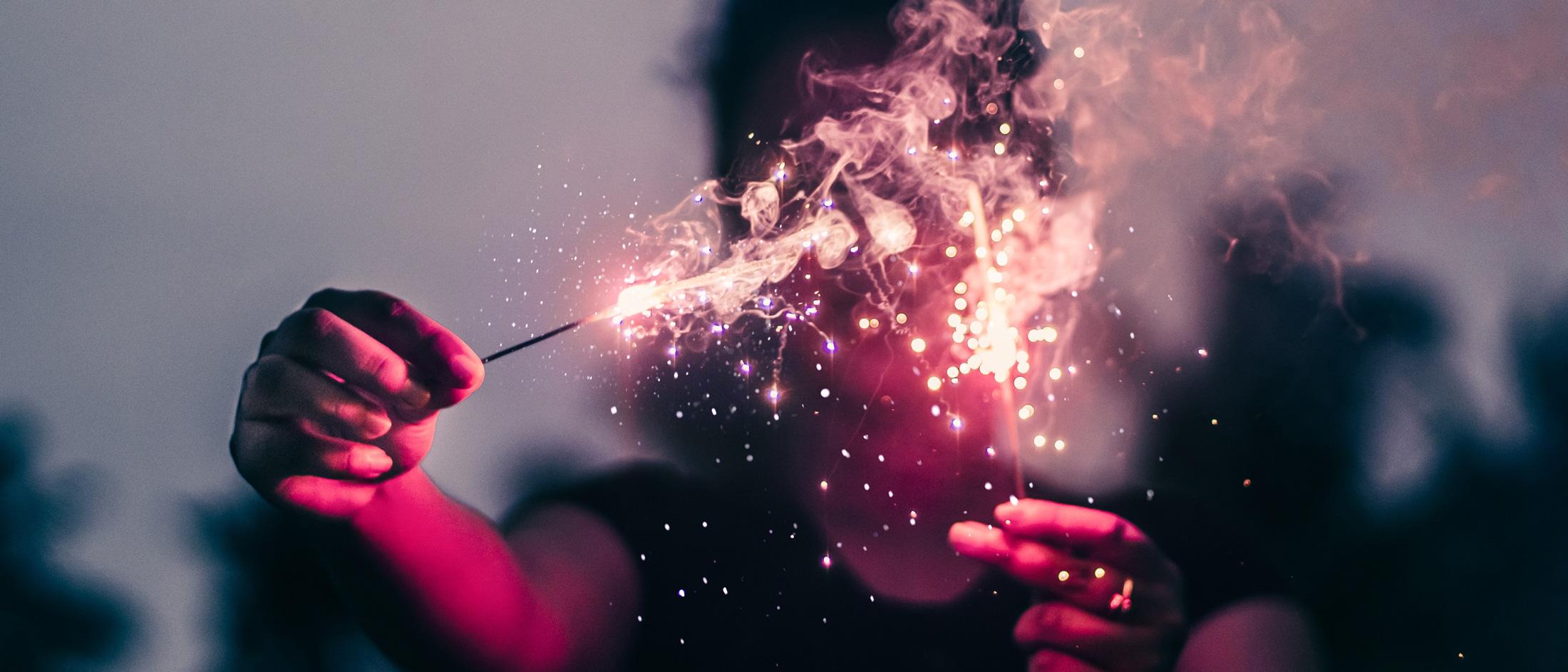 A person holding a sparkler with glowing red sparks and smoke