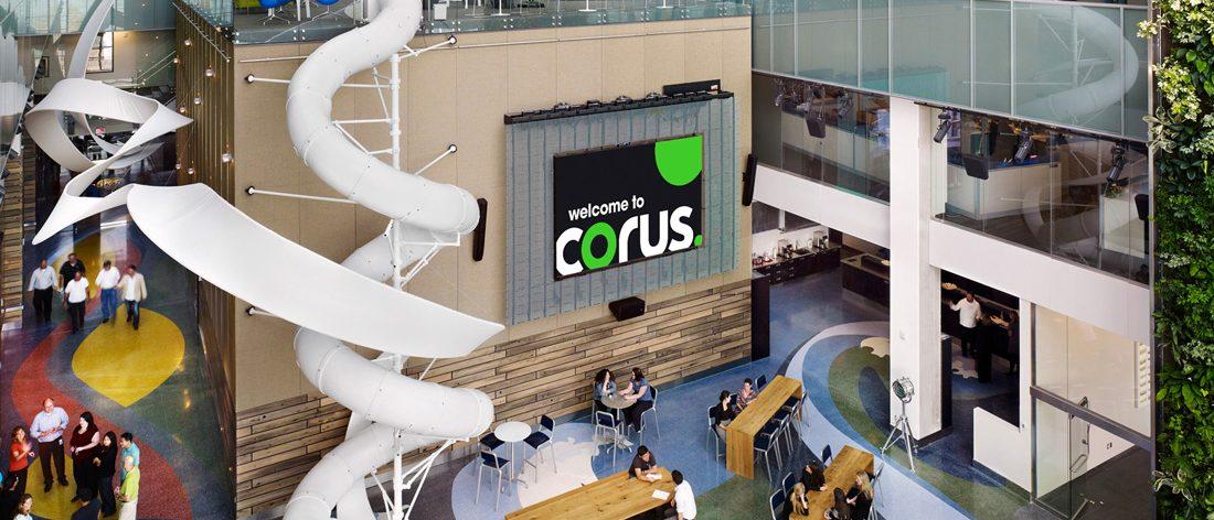 Birds-eye-view from inside Corus Quay, with some people chatting and moving past the cafeteria on the ground floor next to the three-storey tall slide.