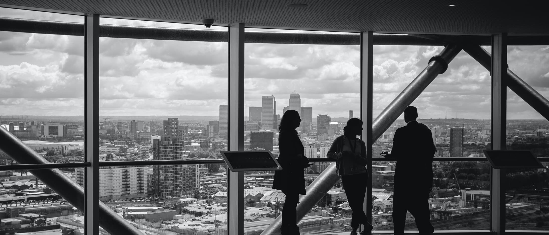3 people standing and looking at a glass window inside a high-rise building